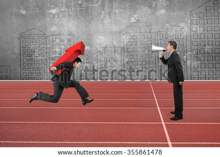 One man using speaker to direct another man carrying 3D red arrow up running on track.