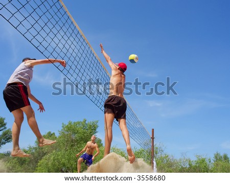 Three men playing beach volleyball - teenager blocks a tall guy over net. Shot near Dnieper river, Ukraine.