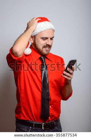 Winter, a business man angry looking at the phone. Corporate party, Christmas hat isolated portrait of a man on a gray background, studio photo.