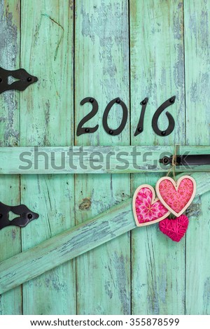 Year 2016 in black iron numbers and red and pink country fabric hearts on antique rustic mint green wood door