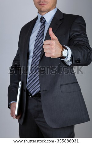 Business man holding laptop and showing thumbs up over gray background. Business success concept