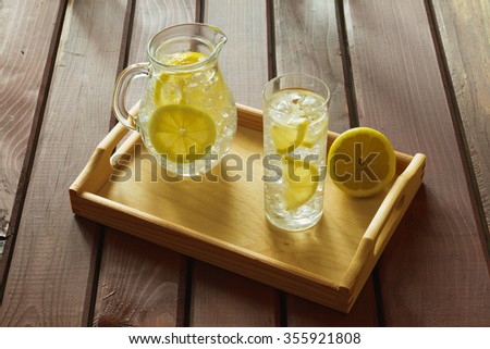 Water drink with lemon on wooden tray with ice and condensation on glass