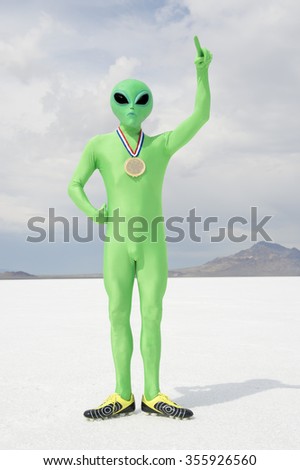 Green alien athlete wearing gold medal standing with number one finger pointing to the sky on stark white planet background