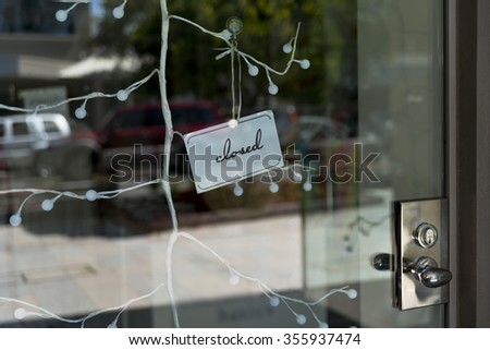Closed sign on glass shop entrance. Cars and street can be seen on glass door reflection. Silver metal door handle and lock. 