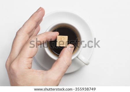 Male hand holding cane sugar cube over cup of black coffee against white background with space for text, top view, focus on sugar Royalty-Free Stock Photo #355938749