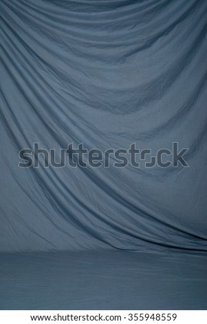 Draped canvas or muslin fabric cloth studio backdrop or background, suitable for use with portraits, products and concepts. Muted blue color. Royalty-Free Stock Photo #355948559