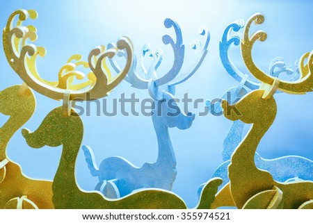 Group of decorated foam reindeer for Christmas holiday with shiny golden and silver color against white backdrop with blue tint.