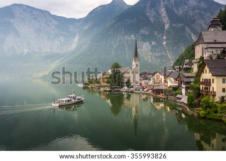 Hallstatt Scenic picture-postcard view of famous mountain village by Lake Hallstatt and Approach Ferry boat with Austrian Flag in the Austrian Alps under Golden Dramatic Sky Sunset in Summer, Austria