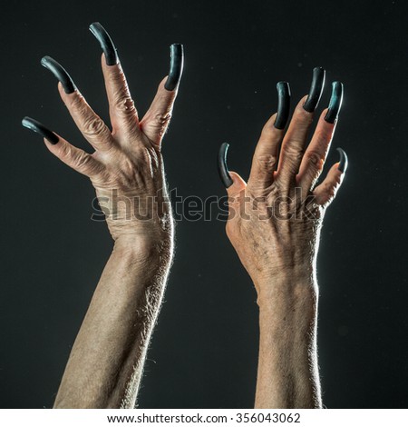 Closeup view of two female old scary mystic hands with long black nails on fingers of witch zomby demon or devil on halloween holiday character in studio indoor on dark background, square picture