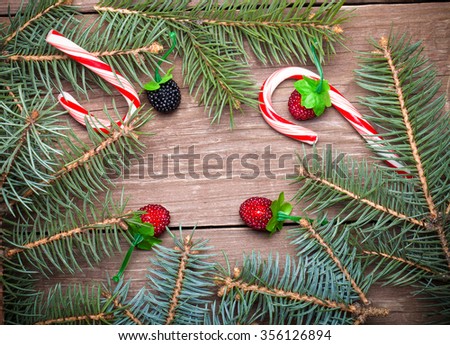 Christmas tree branch, berries and candy canes on a wooden table or board for background. New year theme. Toned.