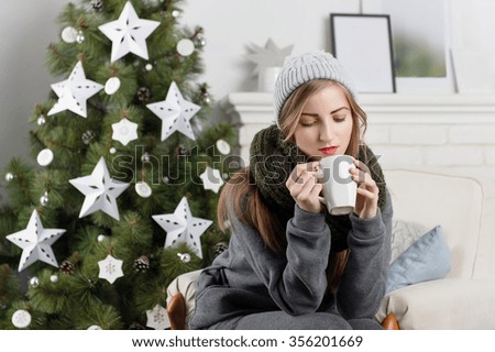 girl sitting in a chair with a cup on a background of the fireplace in the new year