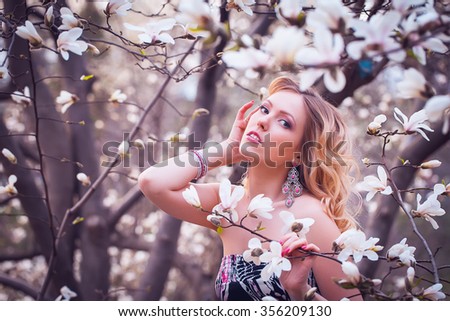Beauty smiling woman near white magnolia in botanical garden