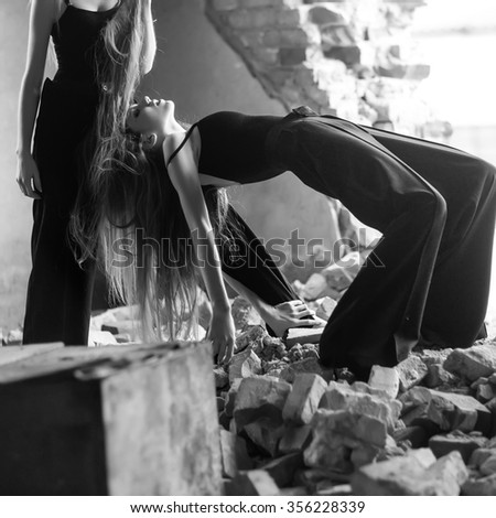 One flexible strange fashionable elegant young woman in black clothes with long hair on building area with broken bricks outdoor black and white, square picture