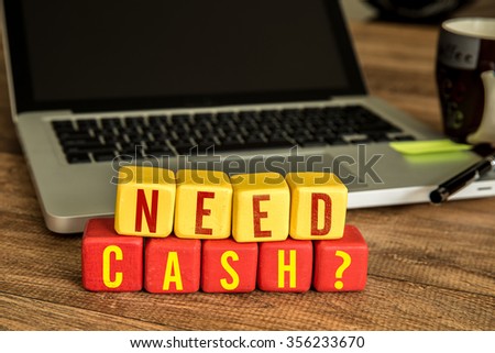 Need Cash? written on a wooden cube in a office desk