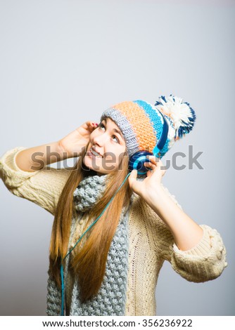 Happy beautiful girl listening to music with big headphones, knit cap, winter concept, photo studio, portrait of a woman isolated on gray background