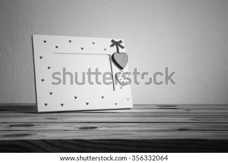 White vintage photo frame with heart on wooden table over wall grunge background, Valentine day concept, black and white