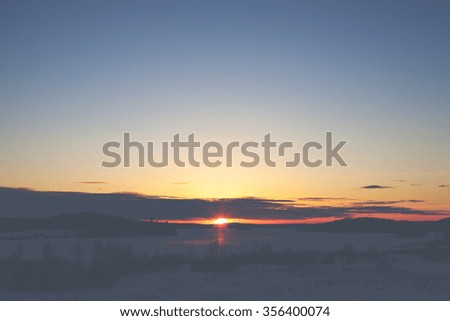 Amazing and colorful sunset in the winter time in Finland. Image taken on a lake and the forest far away is a silhouette. Image has a strong vintage effect applied.