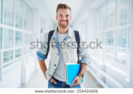 Happy guy with book and touchpad looking at camera Royalty-Free Stock Photo #356426606