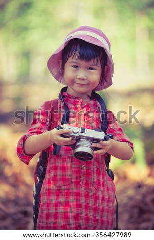 Cute little asian girl with professional digital camera looking at camera and smiling over nature background. Photo in retro style. child in nature. Outdoors portrait.