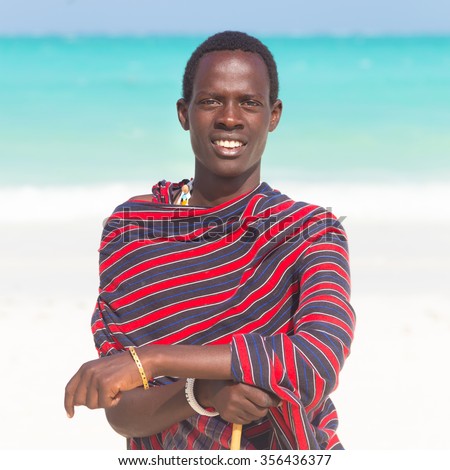 Traditonaly dressed black man on the beach. Maasai warrior on picture perfect tropical sandy beach on Zanzibar, Tanzania, East Africa.