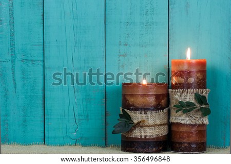 Textured candles with rope and leaves burning by antique rustic teal blue wooden background