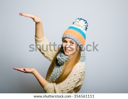 Happy beautiful girl shows a rising trend, knit cap, winter concept, photo studio, portrait of a woman isolated on gray background