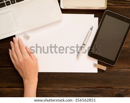 woman's hand writing on white sheets of paper with laptop, tablet, usb memory card and other items on dark wooden background. Business concept.