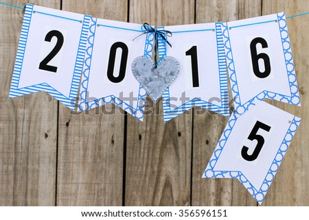 Year 2015 changing to year 2016 with silver tin heart hanging on clothesline with antique rustic wood background