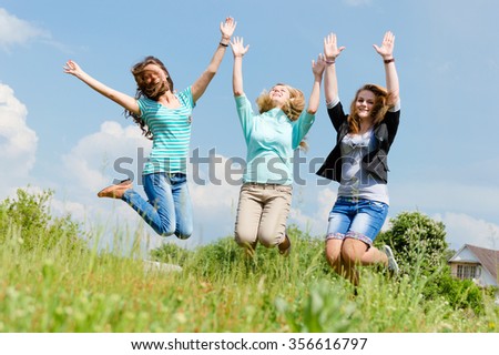 Three beautiful young ladies holding hands jumping on summer field outdoors background