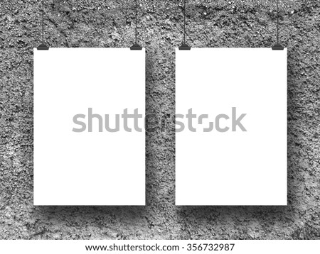 Close-up of two hanged paper sheet frames with clips on rough concrete wall background