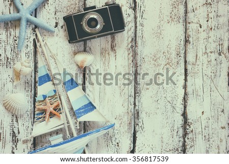 top view image of photo camera, wood boat, sea shells and star fish over wooden table 