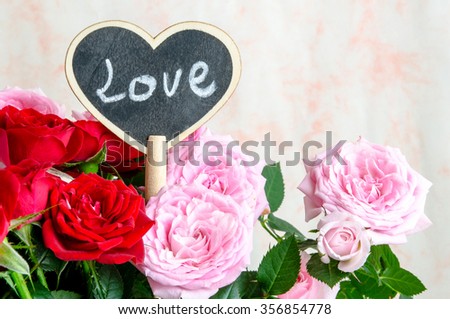 Handmade wooden heart with written word 'love' among red and pink roses