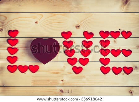 The word "love" lined with little red hearts on wooden background.