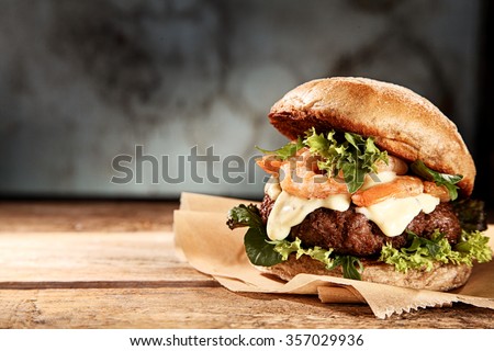 Tasty grilled prawn and beef burger with lettuce and mayonnaise served on pieces of brown paper on a rustic wooden table of counter, with copyspace