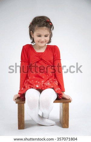 Beautiful little girl dressed in red playing and posing with light grey background 