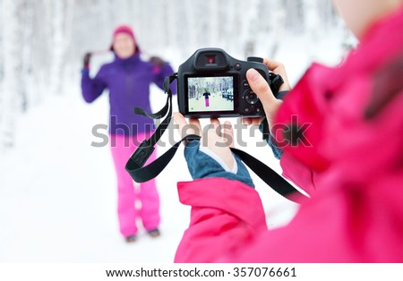 Two girls with a camera taking pictures in snow in winter in a park. Bright jacket. Photographer with the camera. Reflection on the screen