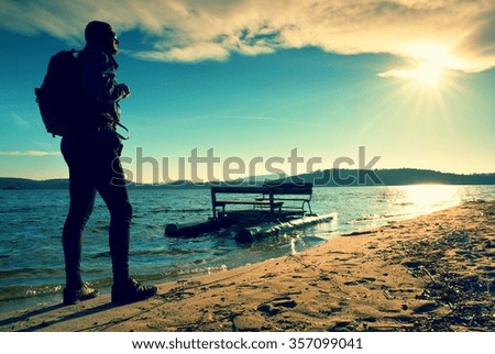 Tall tourist with backpack walk on beach at paddle boat in the sunset. Autumn at se.