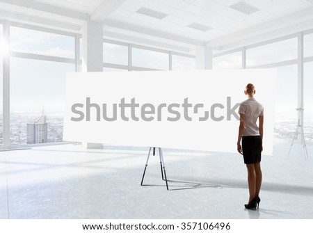 Elegant businesswoman in modern office interior against window panoramic view looking at blank banner
