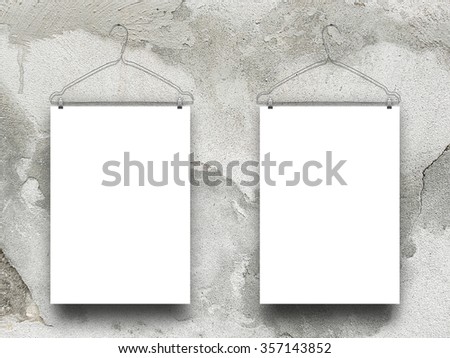 Close-up of two hanged paper sheets with clothes hangers on damaged concrete wall background
