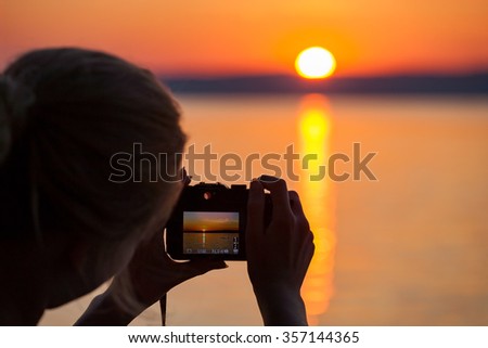 Girl taking photograph of sunset