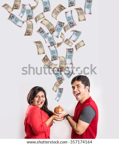 indian couple excited to see currency notes falling from sky to the terracotta money box or piggy bank