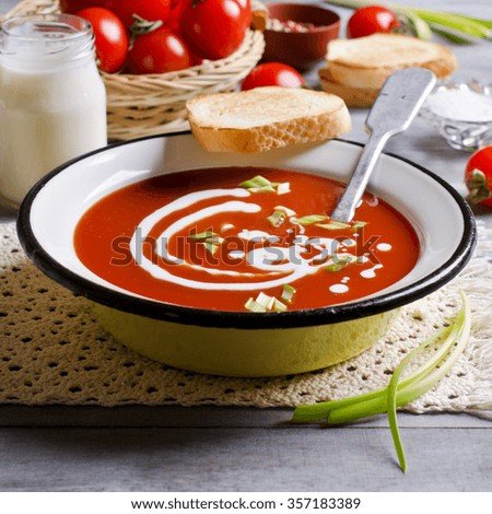 Tomato puree soup with cream in a metal bowl on a wooden background. Selective focus.