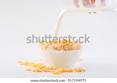 Breakfast dish. Glass of milk is being poured into bowlful of corn flakes. 