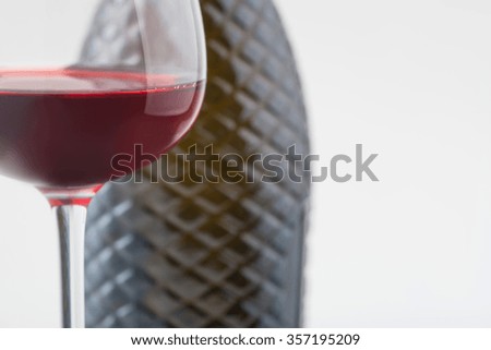 Nice beverage. Glass containing red vine and bottle behind are standing on white surface