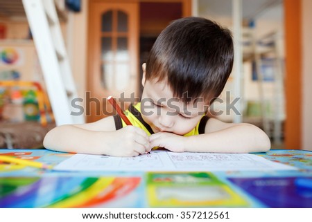 Busy little boy drawing with felt pens at home with colorful interior, three years old.
