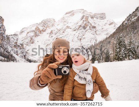 Winter leisure time spent outdoors among snowy peaks can turn the holidays into a fascinating journey. Mother and surprised child checking photos in camera outdoors among snow-capped mountains