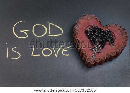 In the picture a rosary iron placed over a heart of red wax, on the left side the inscription "God is Love" made with a crayon.