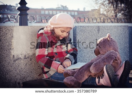 The girl in a checkered coat sitting on a park bench and reading a book  toy Bear. Toning, vignette