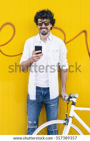utdoor portrait of handsome young man with mobile phone and fixed gear bicycle in the street.