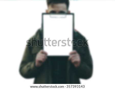 Blurred defocused photo of the yung man holding a white empty paper ion white isolated background
